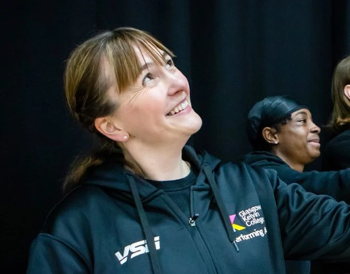 Mhairi Watt, dressed in Glasgow Kelvin College activewear, smiles and gestures while participating in a group activity in a sports hall. Mhairi Watt, dressed in Glasgow Kelvin College activewear, smiles and gestures while participating in a group activity in a sports hall.